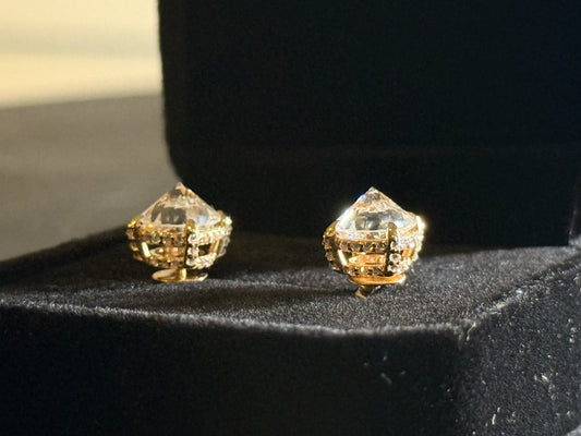Pair of gold and clear gemstone earrings on a black stand.